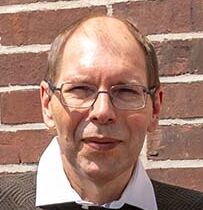 Der erfolgreiche Umschüler André Pardun steht mit verschränkten Armen vor einer geziegelten Hauswand.