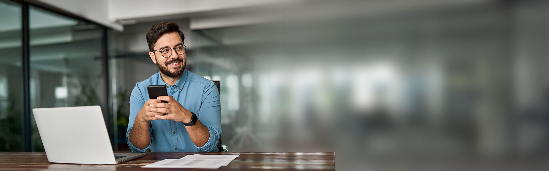 Mann in einem modernen Büro schaut konzentriert auf sein Smartphone.