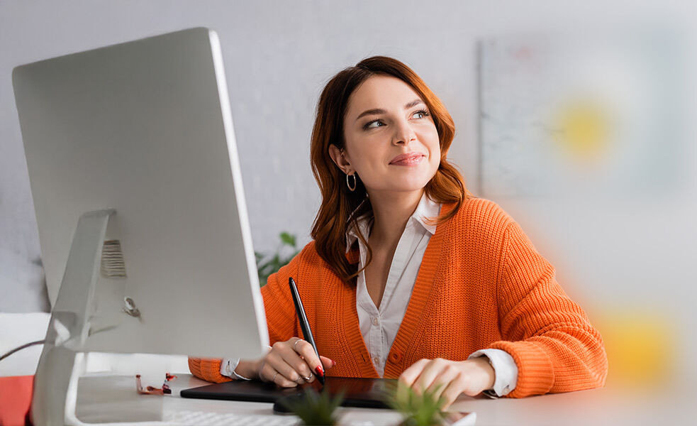 Junge Frau sitzt lächelnd vor einem Computer-Monitor.